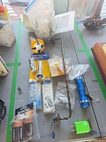 Overview of lot showing pipe cutter, batteries, bulbs, flashlight, USB adapter, screws, auger rod and masking paper