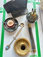 Group shot of all items including chamberstick, bell, spyglass, bookends, spoon, letter opener