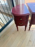 Front view of both red demi-lune nightstands showing drawers, hardware and legs