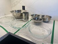Grouping of all stainless bowls, glass bakeware, lid, and flour sifter on countertop