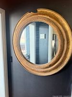 Front view of round gold gilt wood wall mirror, shows missing section at top and overall wear