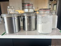 Front view showing stainless-tone cylindrical canisters and smaller glass jars with clamp lids