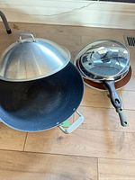 Large black wok with stainless dome lid and additional pans beside