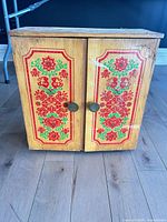 Front view of small painted wood cabinet with floral panels and two doors