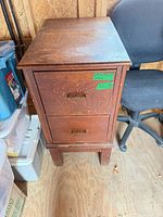 Front view of oak-tone two-drawer file cabinet beside black office chair