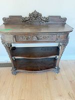Full front view of carved solid wood console table showing drawer, shelves and legs