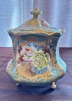 Front view of footed covered jar showing floral panels, gold trim and lid