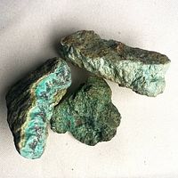 Three green-blue chrysocolla stones on white cloth
