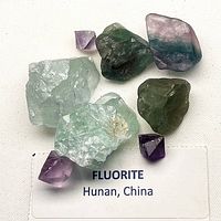 Group of fluorite pieces on white cloth with label 'Fluorite Hunan, China'