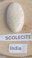 Front view of oval scolecite cabochon on wood background with labels