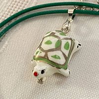 Close-up of white glass turtle pendant on green cord