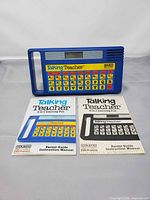 Front view of blue Talking Teacher toy with keypad and display, manuals placed below