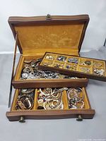 Open wooden jewellery chest showing trays filled with assorted jewellery pieces
