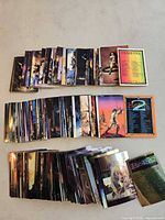 Three stacked trading card sets laid out, some cards fanned to show artwork and checklists