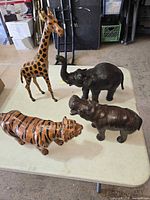 Four leather animal figurines on table: giraffe, elephant, tiger, hippopotamus