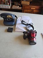 Polaroid 600 camera, Nikon red digital camera with lens cap and charger shown on table
