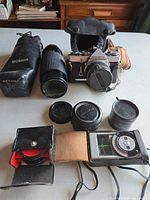 Group shot showing camera with lens, Osawa zoom lens in case, teleconverter, filters, light meter
