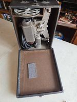 Projector stored inside open carrying case with reel compartment visible