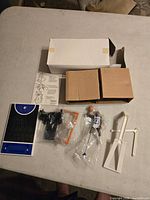 Entire contents laid out: figure in bag, two inner boxes, outer box, court base, plastic parts, instruction sheet