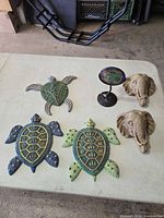 All six items arranged on table: three metal turtle plaques, two elephant sconces, one tabletop holder