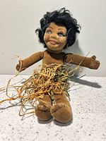 Front view of Norah Wellings velvet doll showing face, body, raffia skirt