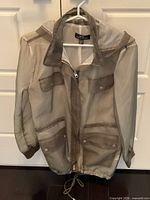 Front view of hooded mesh jacket on hanger showing pockets, zipper, drawstring hem