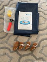Folded blue vinyl splash pad, Marunda booklet, accessory pouch with hose parts and red hand pump, four brown dog boots