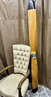 Full view of propeller clock leaning against chair showing scale and wood finish