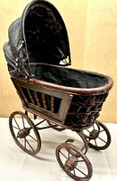 Full view of wooden doll carriage showing wicker sides, metal wheels, fabric canopy
