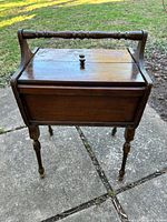 Front view of wooden sewing stand showing drop-leaf lid, knobs, handle and legs