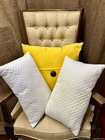 Group shot of yellow pillow and two white quilted pillows on chair