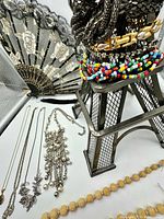 Overall lot showing Eiffel Tower stand, fan, colourful seed bead necklace, bracelets and several necklaces