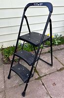 Full view of black 3-step folding stool upright on patio