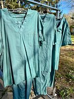 Three sage green scrub sets hanging on rack outdoor