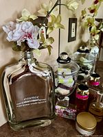 Front view of mirrored factice bottle with faux orchid, branding visible