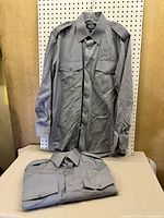 Two gray Opus Canada uniform shirts, one hung, one folded