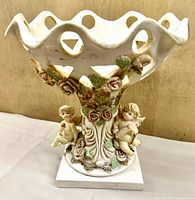 Full view of resin pedestal bowl showing openwork rim, cherubs, roses, and plinth base