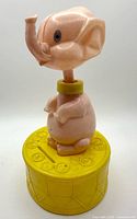 Full view of plastic elephant coin bank, pink figure on yellow base