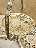 Close view of ornate handle and pierced tray detailing on silver-plated folding server