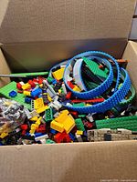 box containing assorted coloured bricks, blue flexible track pieces and various elements