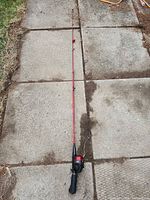 Full view of red and black fishing rod laid on pavement