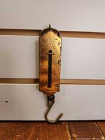 Front view of brass pocket balance scale showing engraved markings, indicator slot, hook