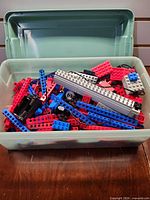 Overview of green tub filled with loose red, blue, grey and black LEGO Technic parts
