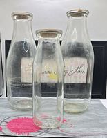 Front view of three clear glass milk bottles with lids