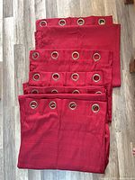 Six stacked red curtain panels displaying grommet headers