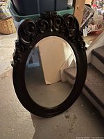 Front view of oval mirror showing ornate scroll frame and reflective glass
