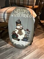 Front of oval wooden sign showing painted snowman and lettering