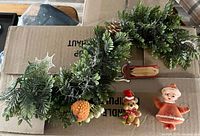Garland, bear ornament, elf ornament, sled, strawberry ornament grouped on box