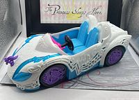 Left front and side view of the white convertible car showing purple wheel, blue accents, hood ornament and molded decorative patterns