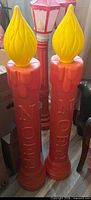 Two tall red NOEL candles with yellow flames; one cord visible